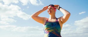 A woman in a vibrant swimsuit stands confidently on the beach, embodying strength and resilience in managing chronic pain through exercise.