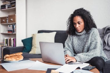 A curly haired black woman browsing through social media networks on her laptop.