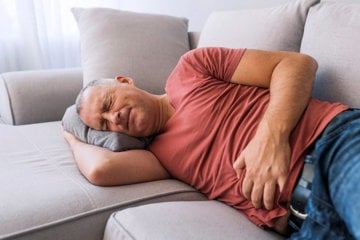 Man lying on the sofa struggling with an intense stomach ache 