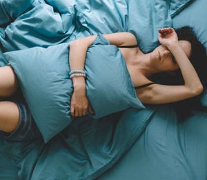 A woman lying on her bed covering her eyes with her arm in frustration because of the constraints placed on her by her chronic illnessA woman lying on her bed covering her eyes with her arm in frustration because of the constraints placed on her by her chronic illness