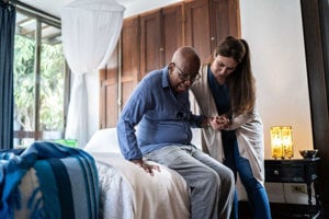 Female caregiver helping her loved one out of bed, feeling happier as she has learned to ask for caregiving help