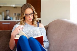 Female family caregiver reading book on sofa with a hot drink practicing self-care