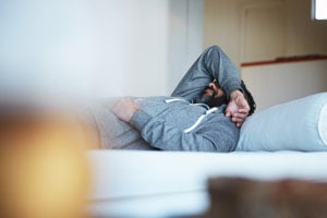 Man covering his face with arm on bed, struggling with depression.