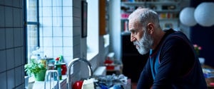 Stressed caregiver looks out of window as he considers all that lies ahead for him that day with his loved one and daughter