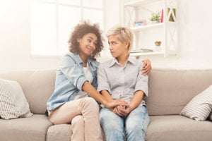 Two friends sitting on couch, one looking unconvinced by what the other is saying.