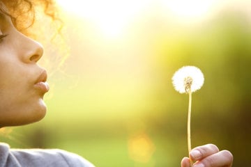 Woman blowing a dandelion in the summer air.