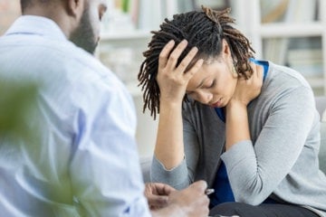 A woman sits at a desk, her head resting in her hands, reflecting on her thoughts and emotions.