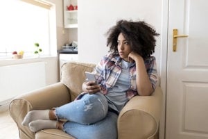 Depressed woman sitting on the couch with her phone in her hand