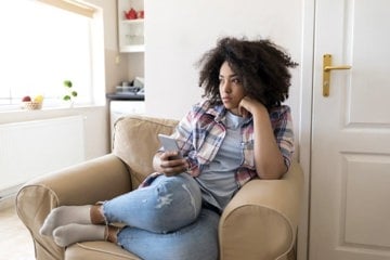 Depressed woman sitting on the couch with her phone in her hand