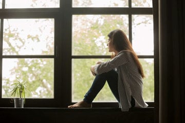 Woman sitting on windowsill, thinking about her anxiety triggers