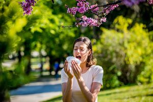 Woman sneezing due to pollen allergies under a blossom tree