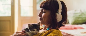 A woman wearing headphones sits peacefully with a cat, embodying self-care and mindfulness in a digital space.