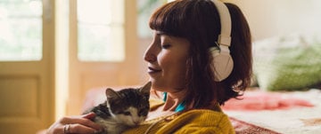 A woman wearing headphones sits peacefully with a cat, embodying self-care and mindfulness in a digital space.