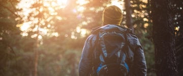 A person with a backpack walks through a lush forest, embodying resilience and adventure despite Huntington’s Disease.