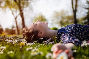 Woman lying down in a daisy field, feeling relieved from the anxiety of migraine