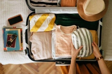 Woman packing the essentials for a migraine-friendly holiday including sunglasses and hat