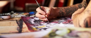 A tattooed man focused on painting on paper, symbolizing creativity and expression in the context of understanding depression.