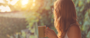 A woman enjoys a warm coffee mug as she gazes at a beautiful sunset, reflecting on self-isolation and personal growth.