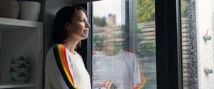 A woman gazes out a rain-soaked window, reflecting on her journey with Huntington's disease and survival after COVID-19.