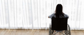 A woman in a wheelchair gazes thoughtfully out the window, reflecting on her surroundings and emotions.