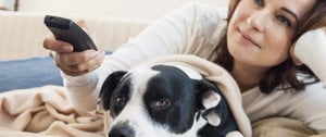 A woman relaxes on a couch with a dog, illustrating the calming effect pets can have on stress and anxiety.